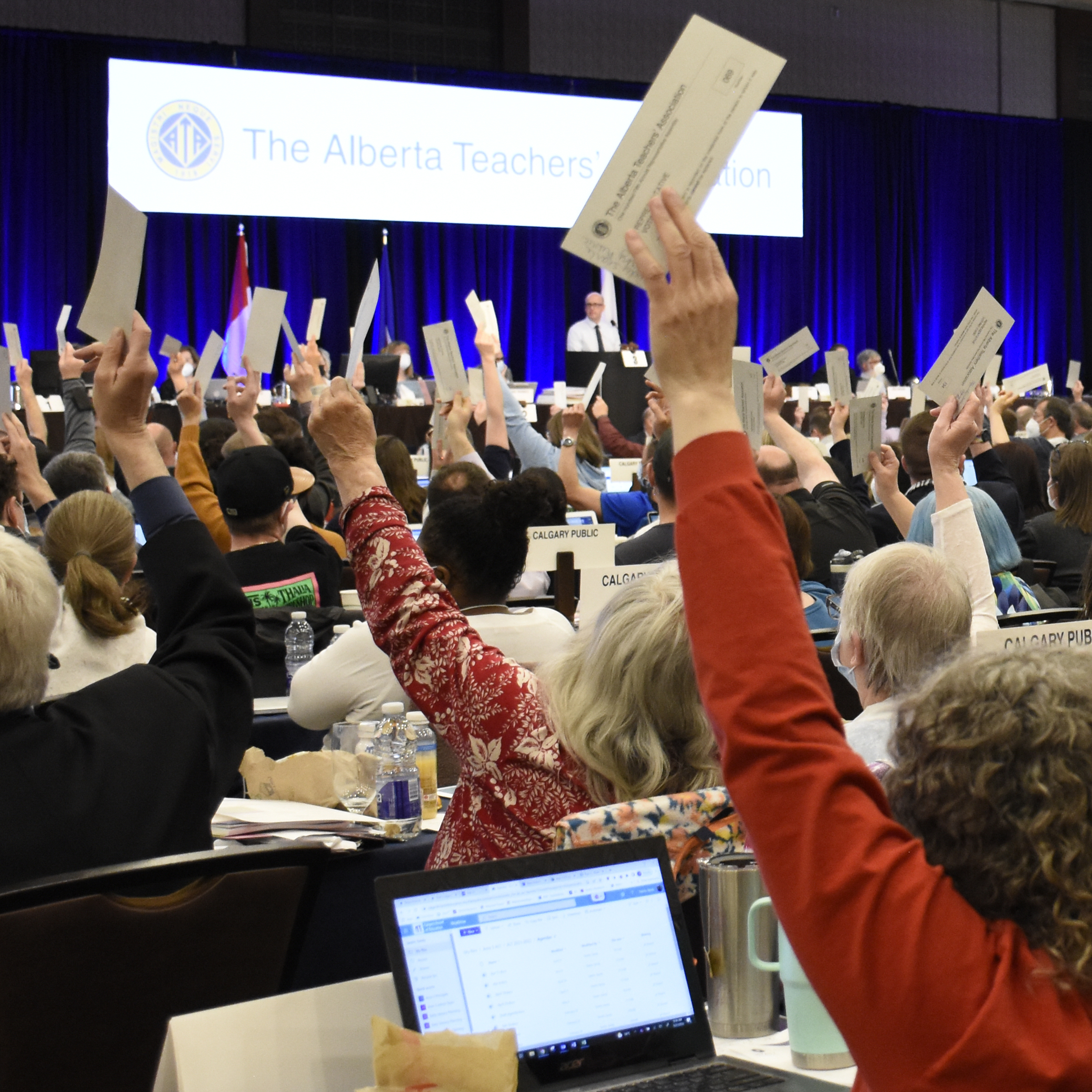 Attendees at annual assembly vote with arms raised and tickets in hand.