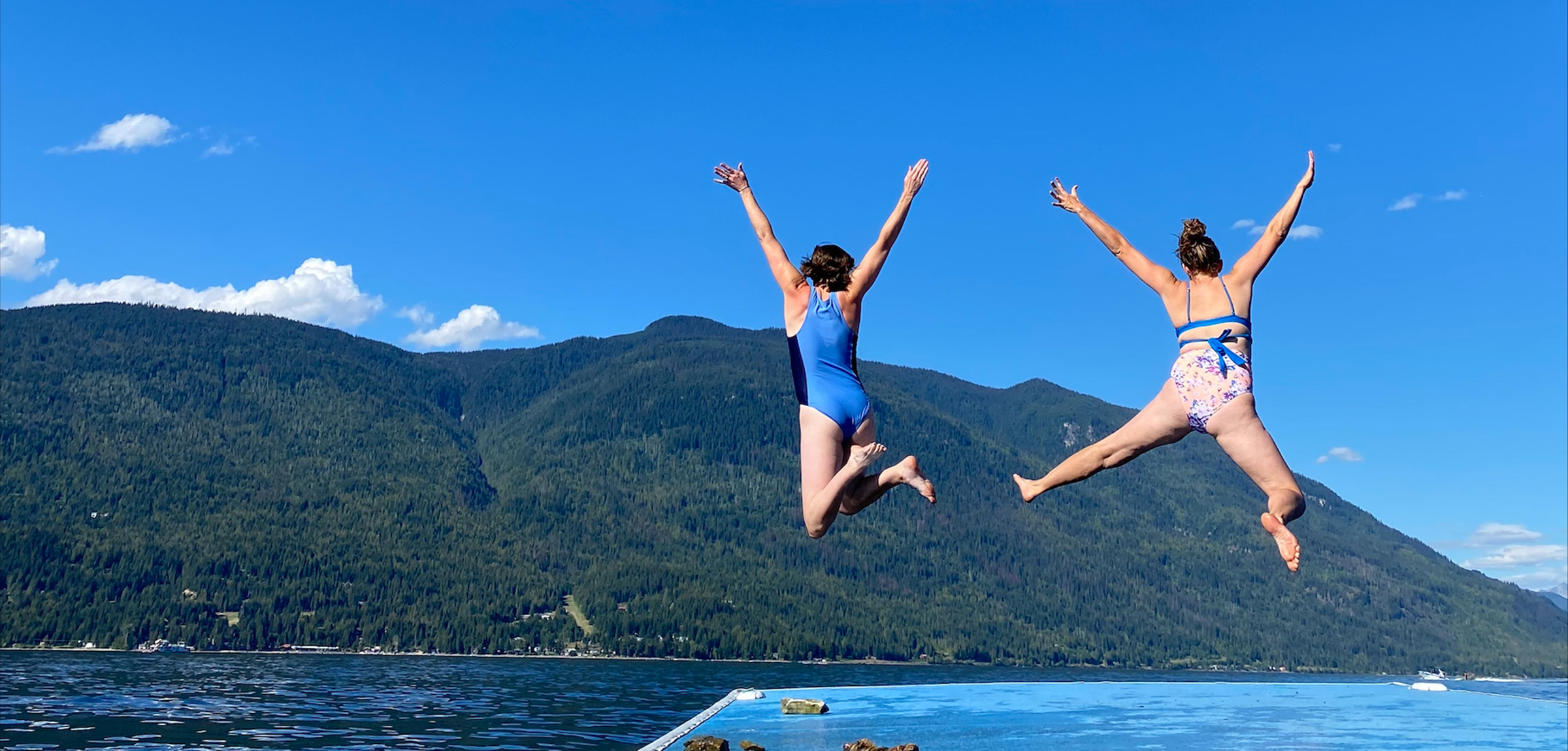 Two women jumping into an Okanagan lake under a blue sky