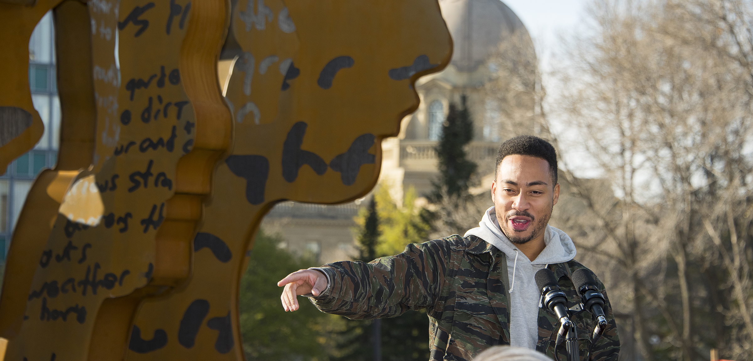 Rapper Cadence Weapon standing in front of the 100th Anniversary sculpture at the Alberta Legislature 