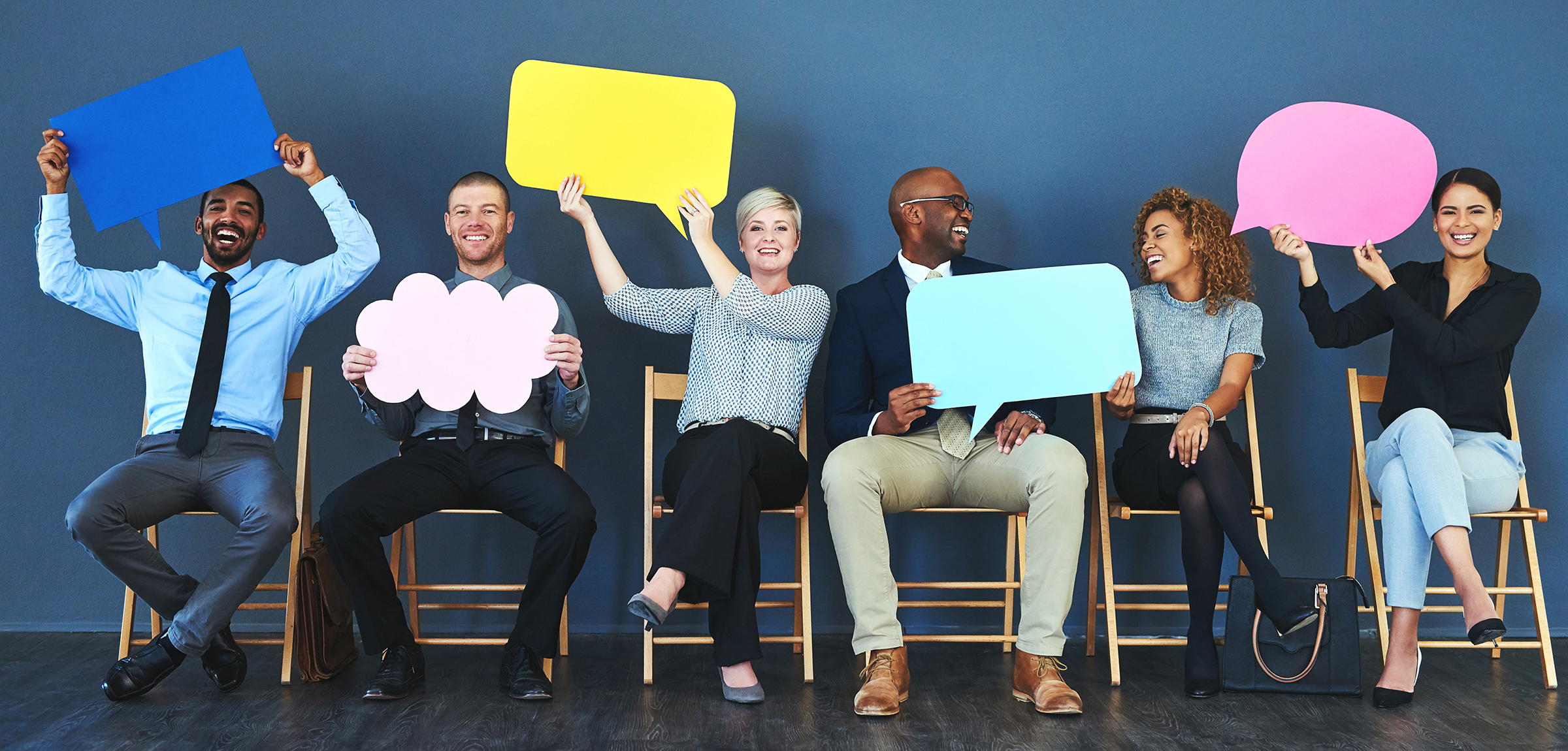 Group of adults sitting on chairs holding blank speech bubbles made of coloured paper