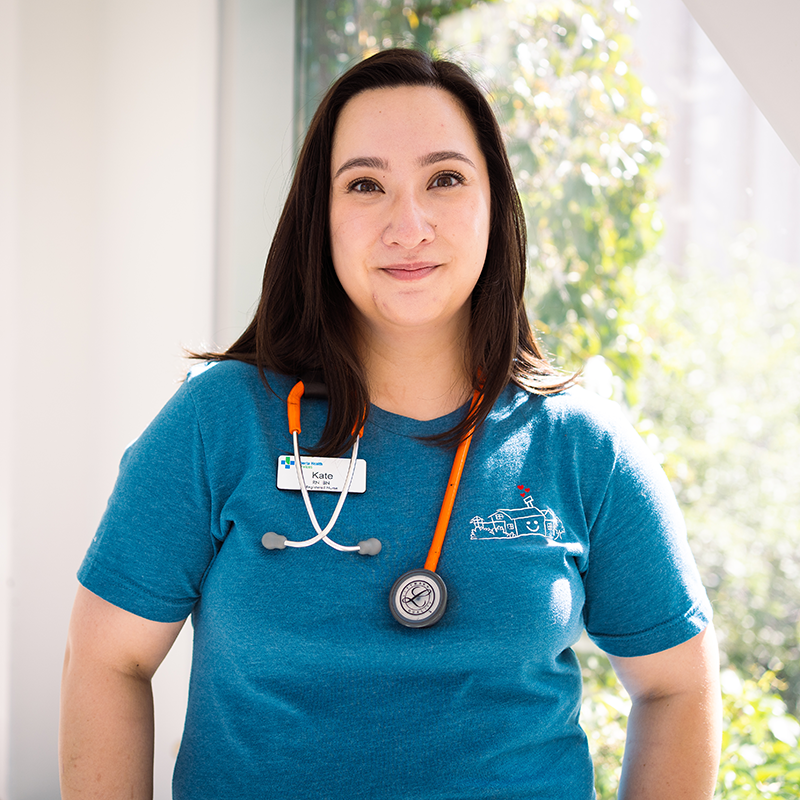 Asian Canadian women in blue teacher stands in front of a window with an orange stethoscope around her neck.