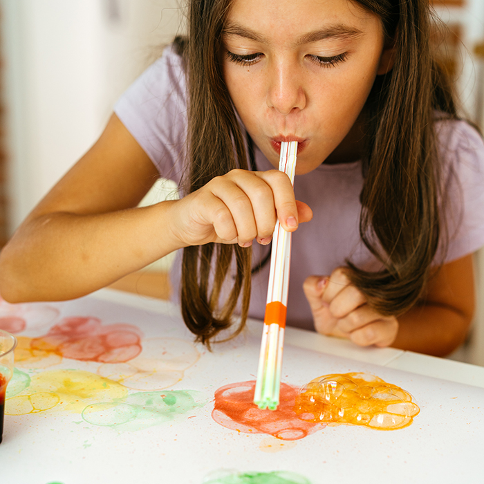 Girl blowing coloured bubbles onto a sheet of paper