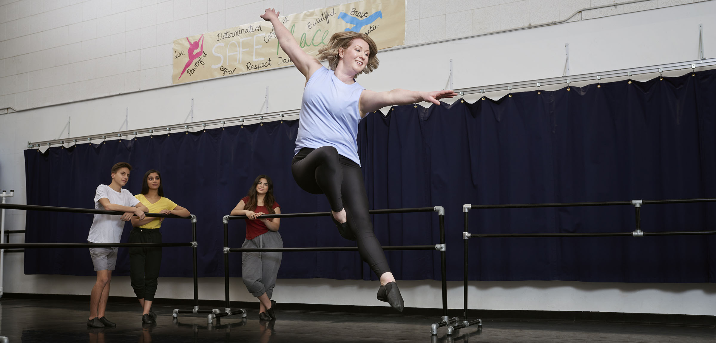 Dancer leaping in a studio with three student watching