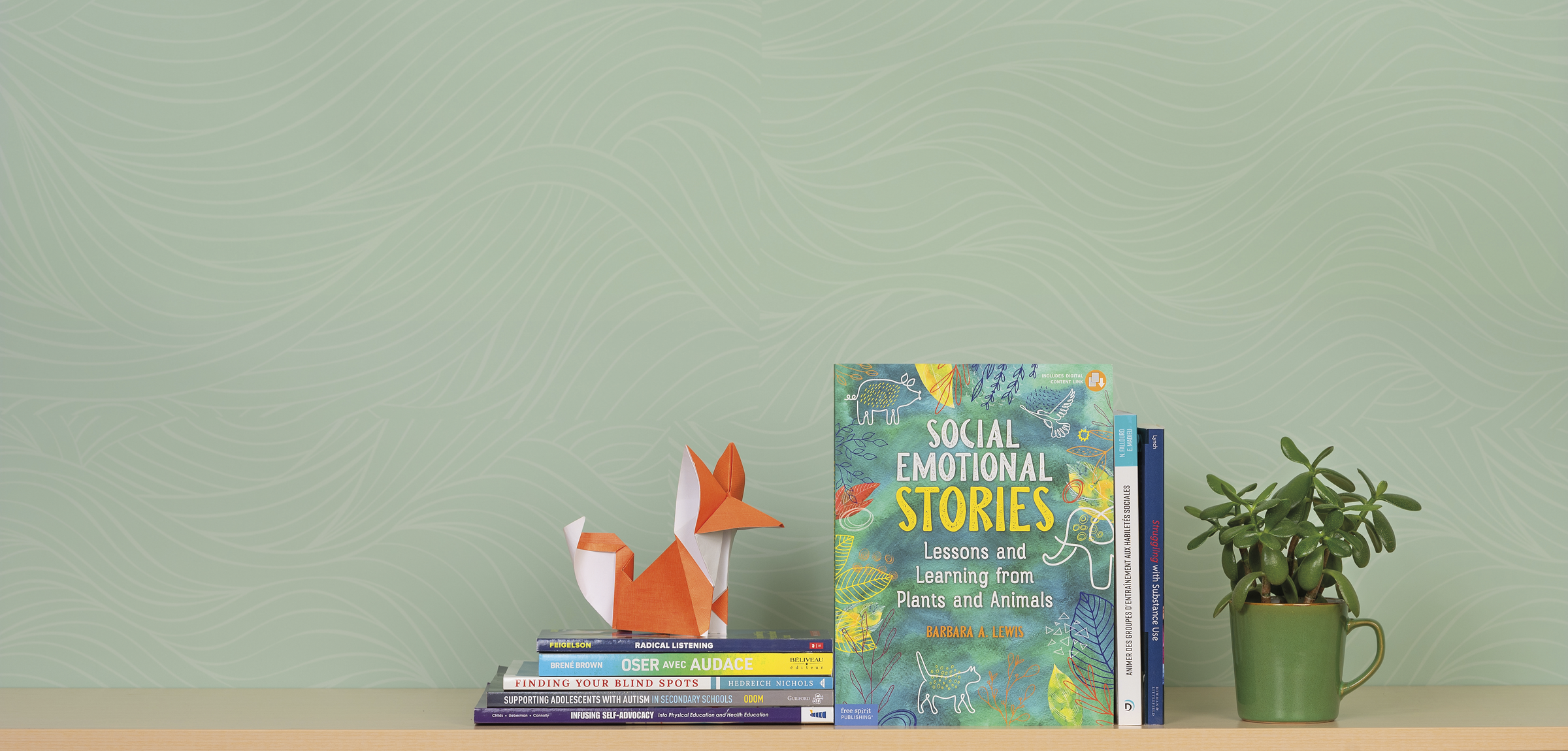 A green wall with 8 books in front of it. A plant in a coffee cup stands on one side and an origami fox on the other side.