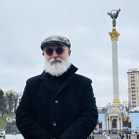 Man in a plaid cap and white beard stands infront of Independence Monument in Kyiv 