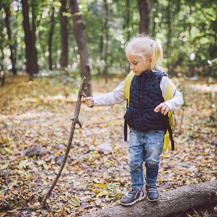 A young girl plays on a log in the forest