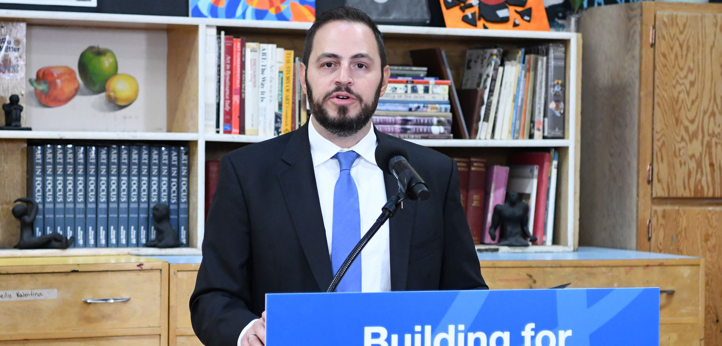 Man wearing blue tie speaks and a podium with sign reading Building for the Future