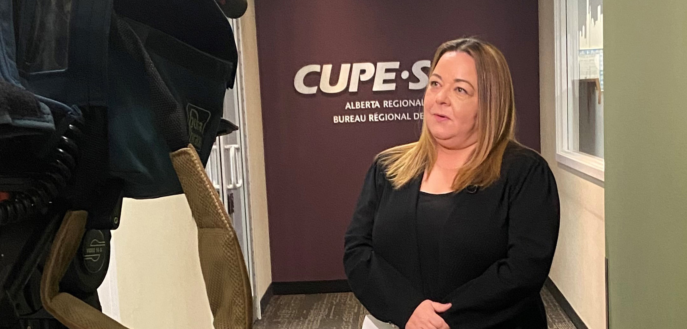 women in black blazer holding a sheet of paper infront of the CUPE logo