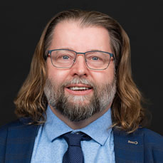 Man with shoulder length hair wearing a blue suit and glasses