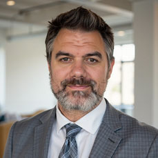 Portrait of man with salt and pepper hair and beard in a grey suit