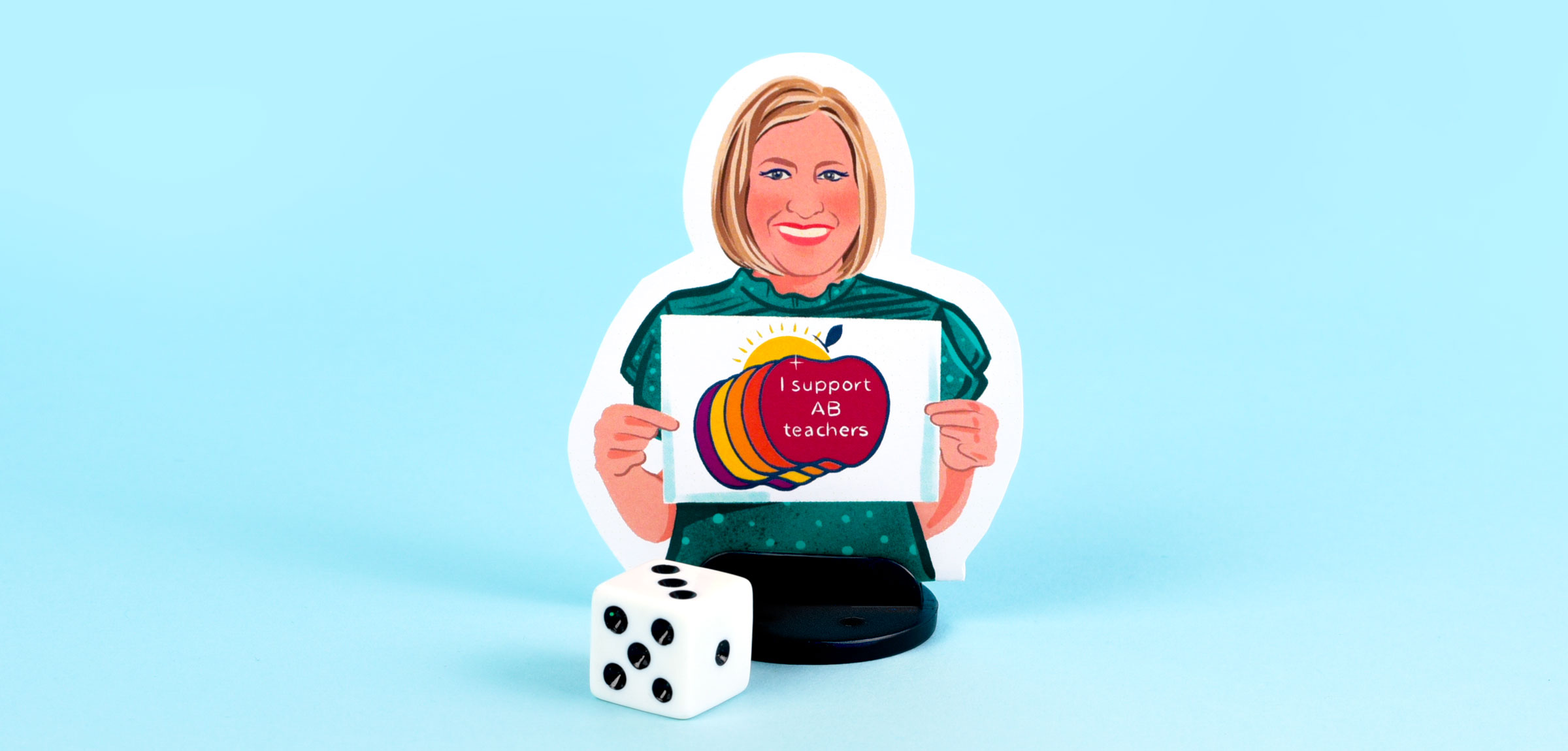 Melanie Buckley An illustrated boardgame player piece sits on a blue background in front of a die. The illustration of Melanie shows her with a blonde bob hairstyle, wearing a green short-sleeved shirt, holding a "I support AB teachers" graphic.