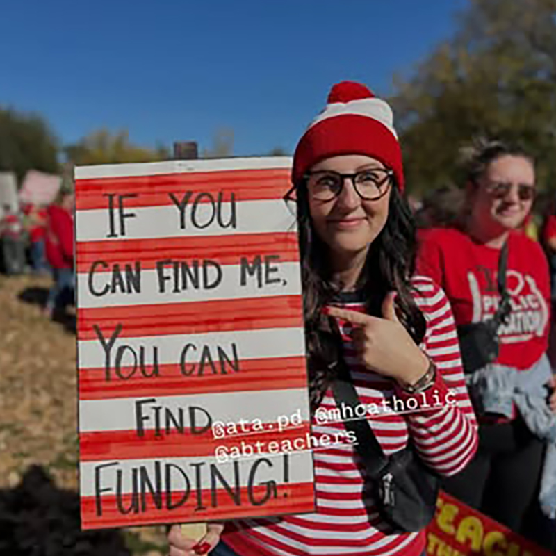A person wearing a Where's Waldo costume holding a sign