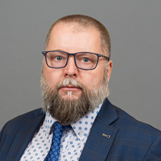 A beared man wearing glasses and a blue tie