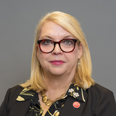 A blonde woman wearing glasses with a closed mouth smile