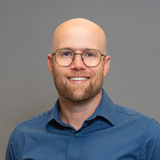 A smiling bald man with a beard and glasses