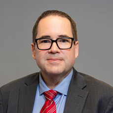 A smiling, brown haired man with glasses