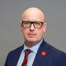 A bald man in a red tie and black glasses