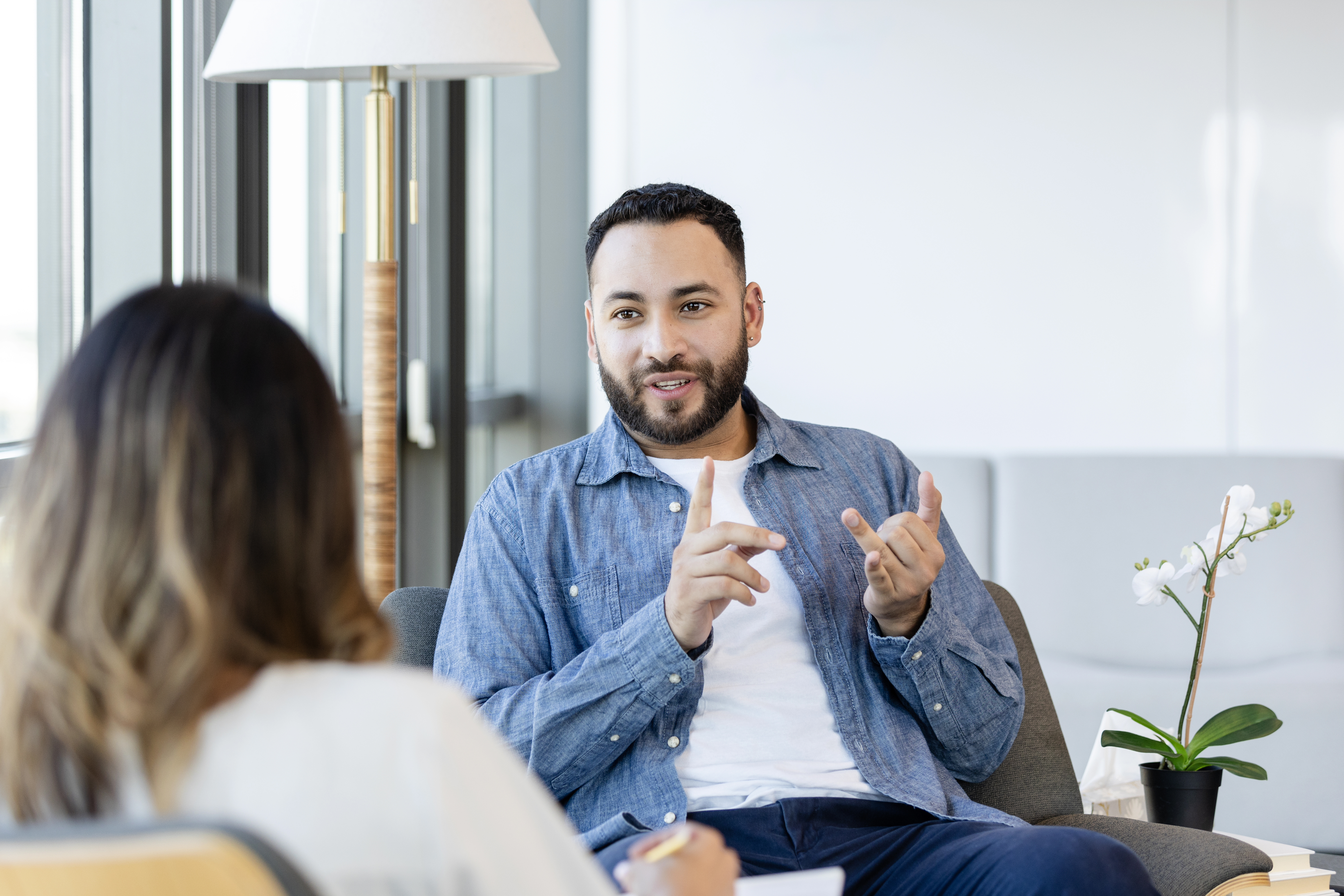 Young man with beard wearing a denim shirt talks with a women in a white shirt