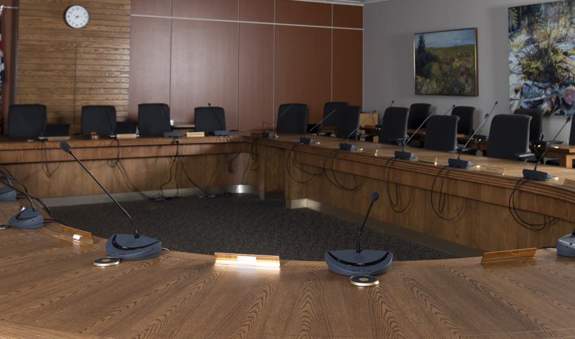 Provincial Executive Council chamber a large round wooden desk lined with microphones and chairs facing the centre.