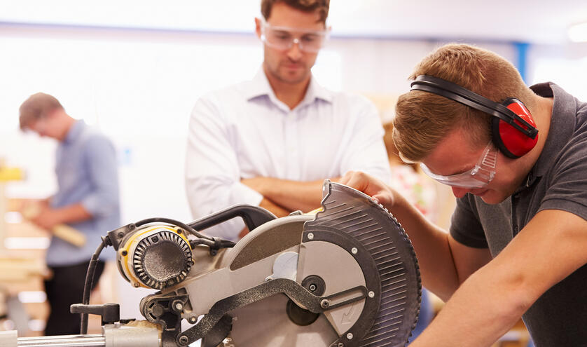 Man looking over student using saw