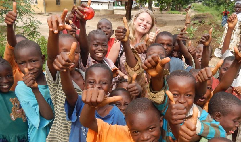 African school children posing with their thumbs up with a teacher from abroad