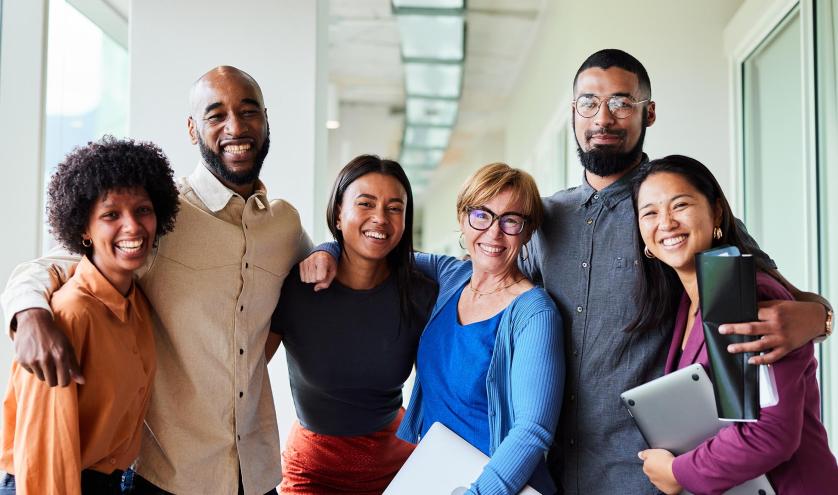 Diverse smiling adults standing with arms around each other in a hallway