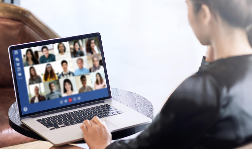 A person wearing a black blouse sitting in front of a laptop screen that has 15 faces on it, all people part of an online meeting