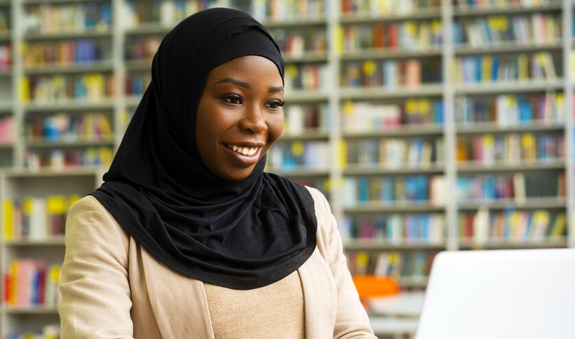 A woman in a hijab using a laptop in a library. 