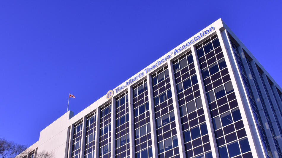 A blue sky background free of clouds. In the foreground is a white building with columns of blue windows. The canadian flag flies from the top of the building. The ATA logo and the text "Alberta Teachers' Association" are also on the front facade.