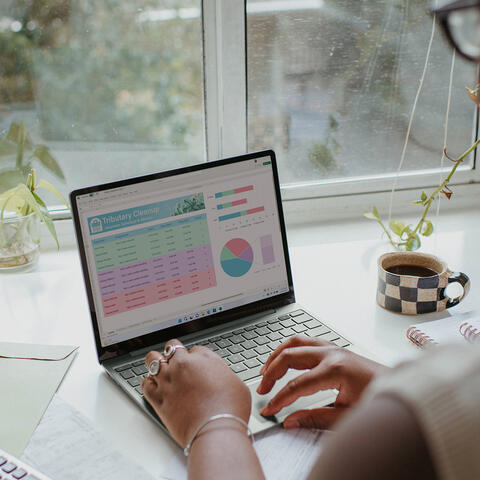 Women of colour looking at finances on laptop next to a window.