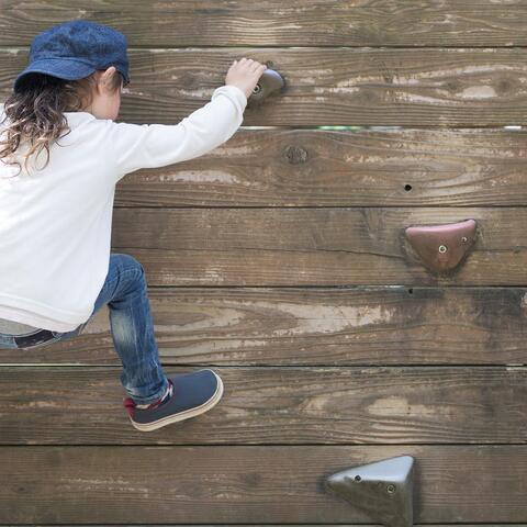 Young child climbing a wall with grips wearing blue jeans, a hat and white shirt