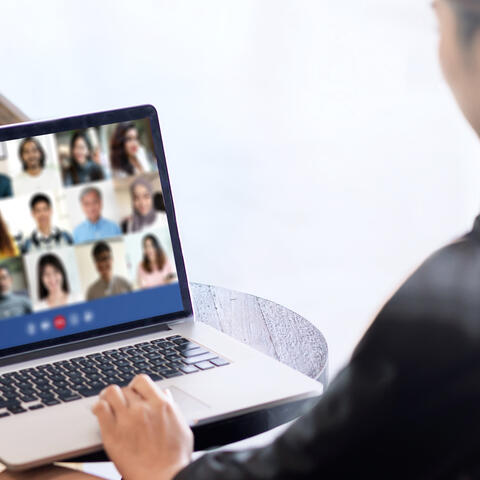 A person wearing a black blouse sitting in front of a laptop screen that has 15 faces on it, all people part of an online meeting
