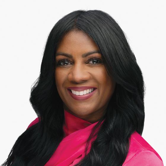 Portrait of a smiling black women with long black hair in a fuscia blouse.