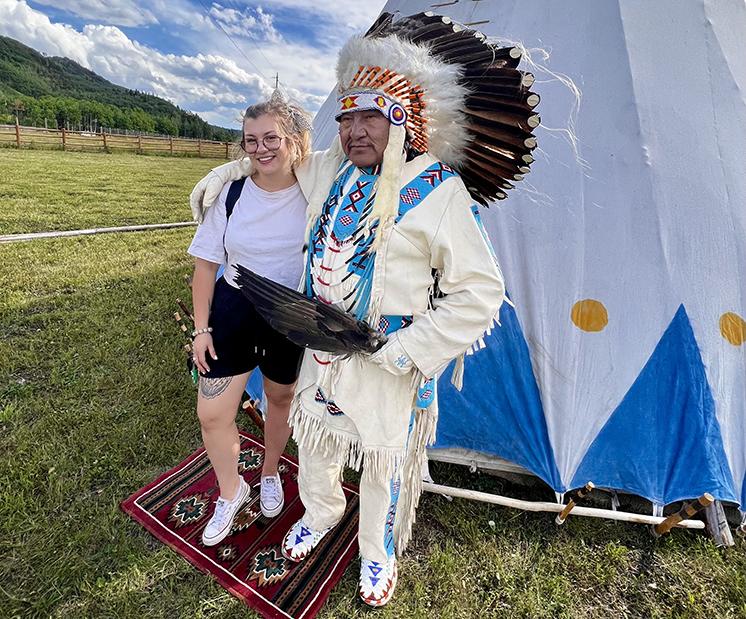 Women and Indigenous elder standing in front of a teepee with hands around each other's backs