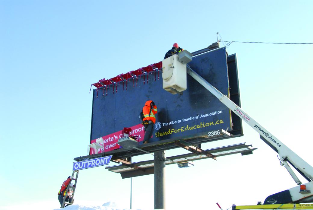 Crew using a crane to install chairs on a billboard