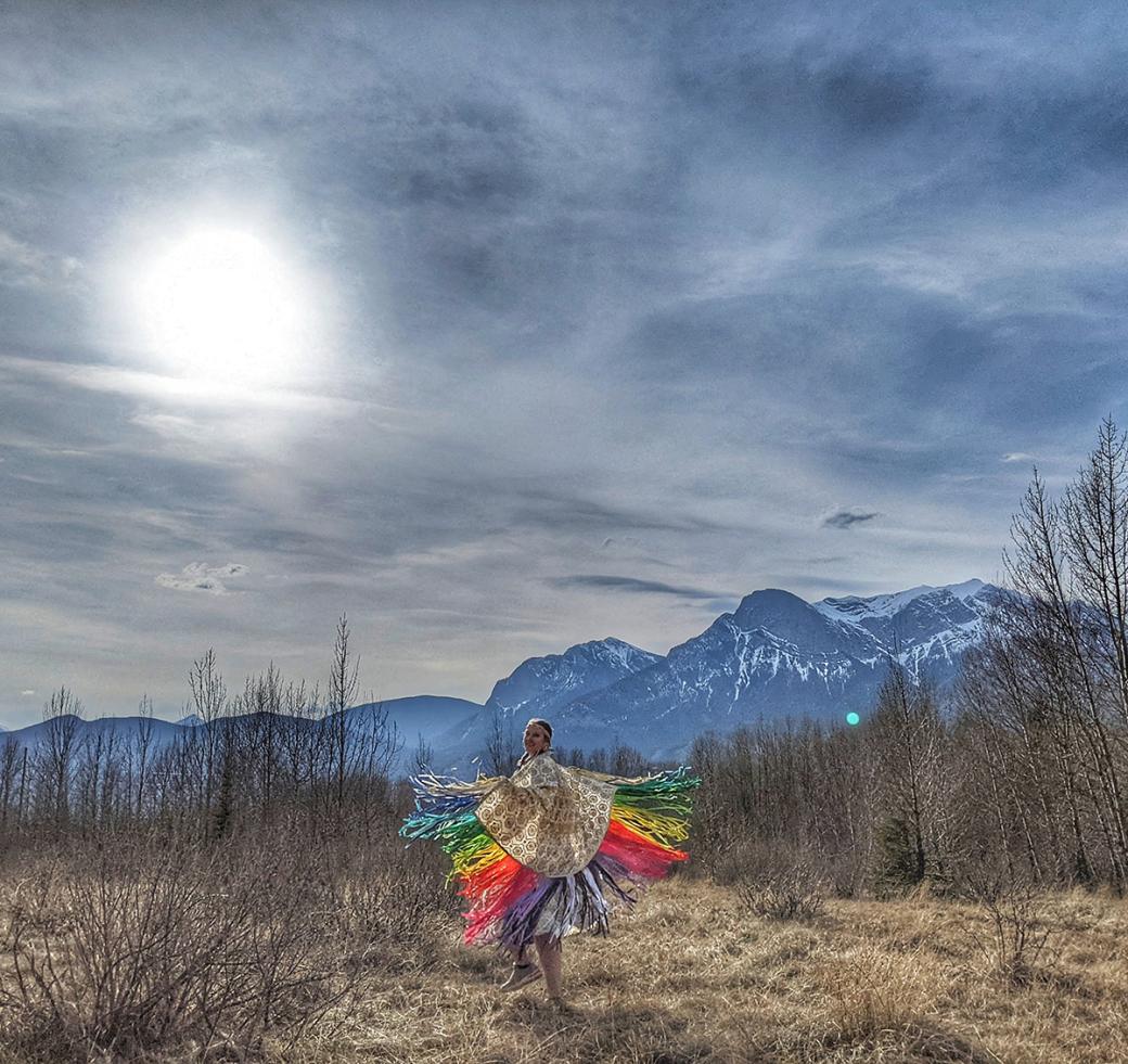 Indigenous dancer, dancing in a field with mountains and sun in the background