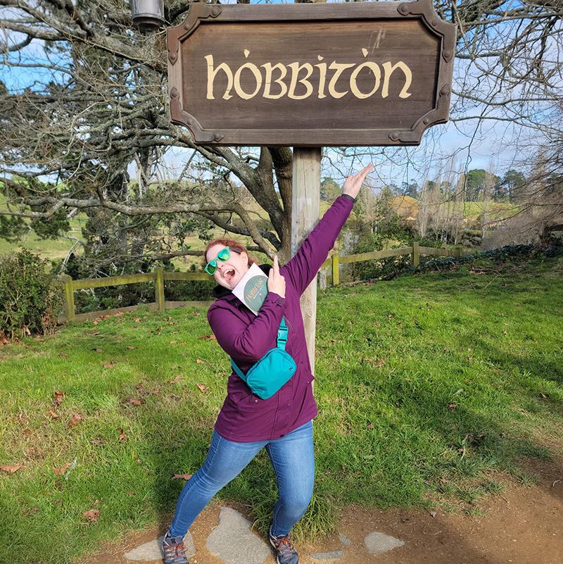 A woman standing in front of a sign that says Hobbiton