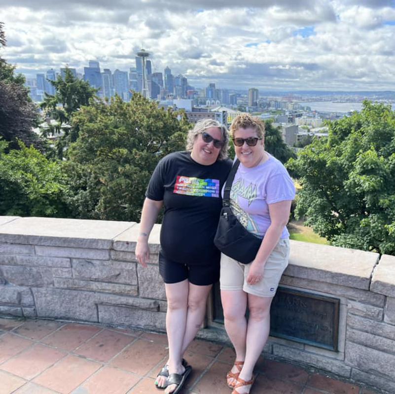 Two woman standing on an outlook with the Seattle skyline behind them.
