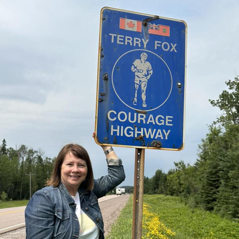 A woman standing next to a Terry Fox Courage Highway sign