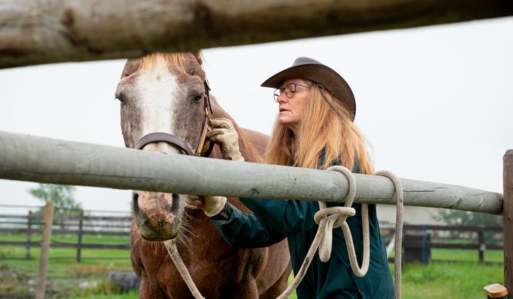 Women in cowboy hat adjusting bridle straps on a horse