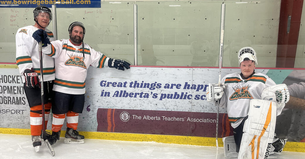 Three hockey players stand by an ATA rink-side ad