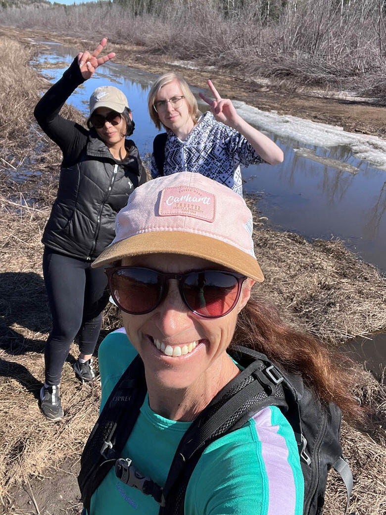 Three women posing for a picture on a hike near a river