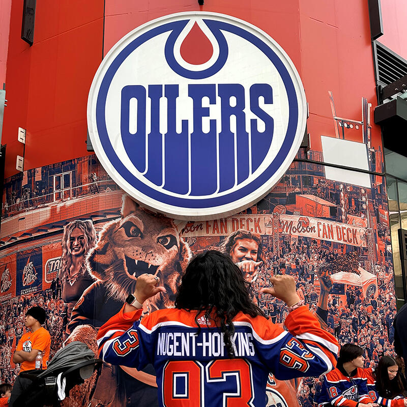 A woman shows the back of her Oilers jersey in front of an Oilers mural