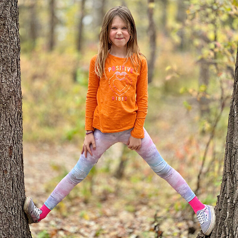 A young girls stands between two trees