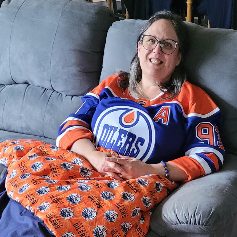 A woman sits on a couch wearing an Oilers jersey covered with an Oilers blanket