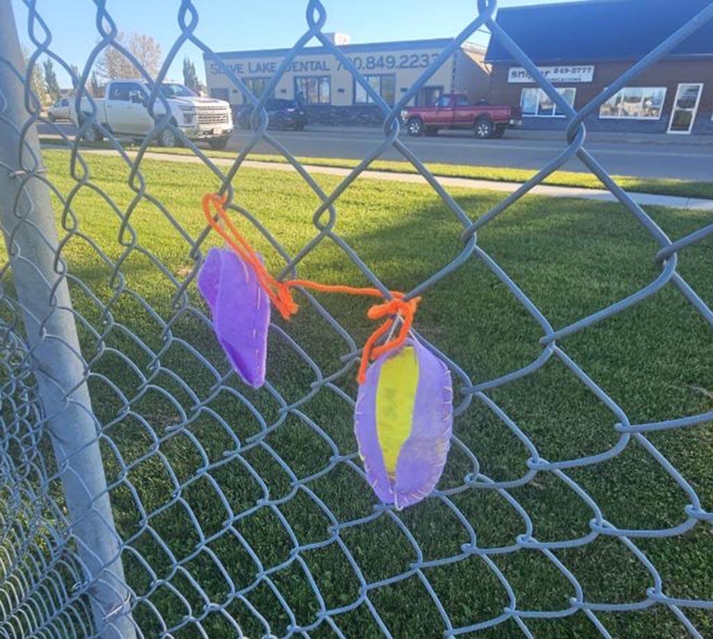 Moccasin's made by students hang on a chain link fence