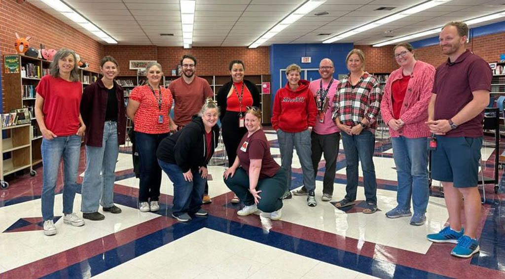 A groups of teachers in a classroom showing off their red shirts