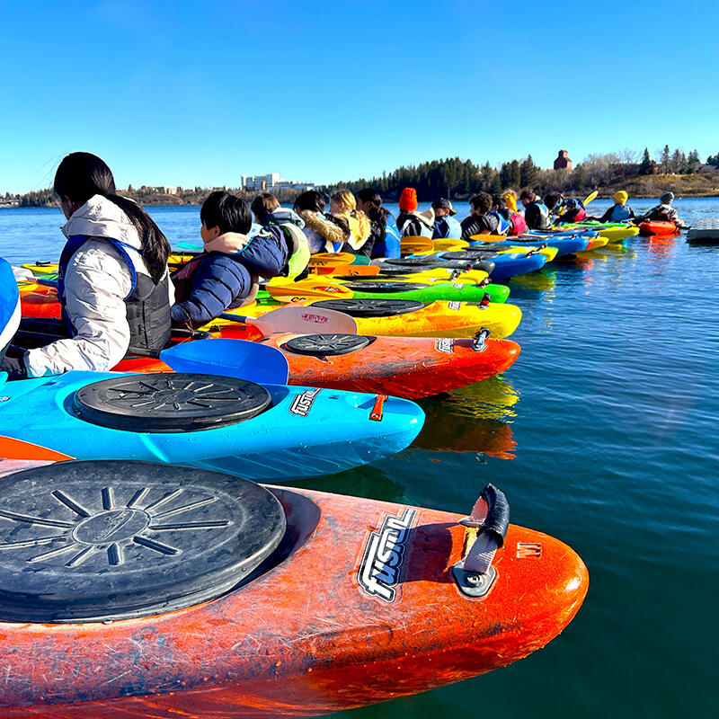 A row of students sitting in brightly-coloured kayaks