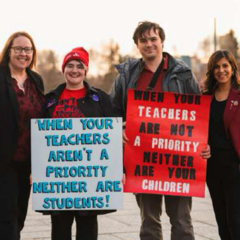 Two individuals holding signs while standing with their MLAs