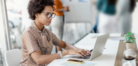 A Black woman with an afro sits at a desk in front of her laptop